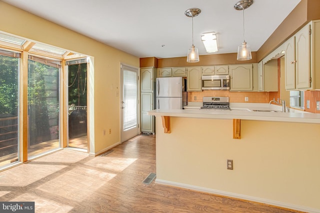 kitchen with appliances with stainless steel finishes, hanging light fixtures, a sink, a peninsula, and light wood-style flooring