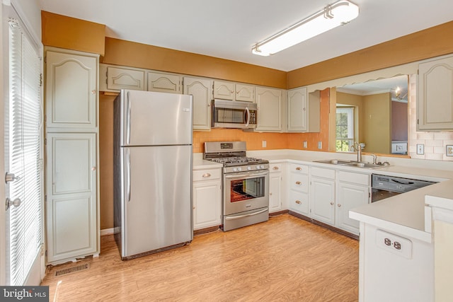 kitchen with appliances with stainless steel finishes, a sink, light wood-style floors, light countertops, and decorative backsplash
