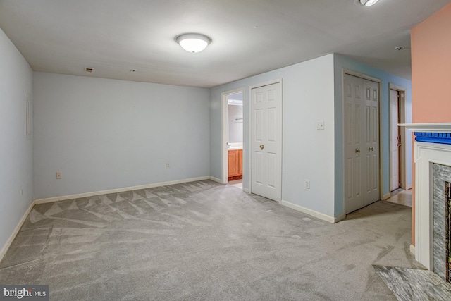 unfurnished bedroom featuring baseboards, carpet flooring, ensuite bathroom, and a fireplace