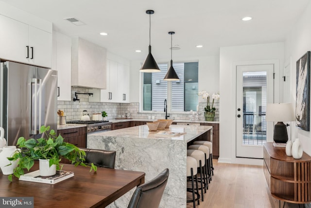 kitchen with a breakfast bar area, high quality fridge, decorative backsplash, white cabinetry, and light wood-type flooring