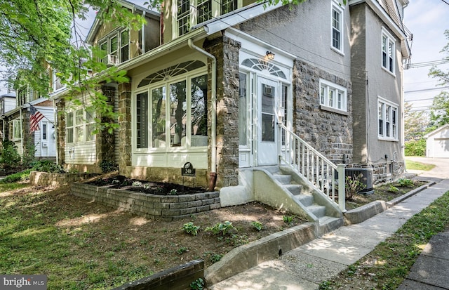 view of property exterior featuring central air condition unit, entry steps, stone siding, and a garage