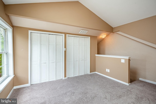 unfurnished bedroom featuring lofted ceiling, multiple windows, visible vents, and two closets