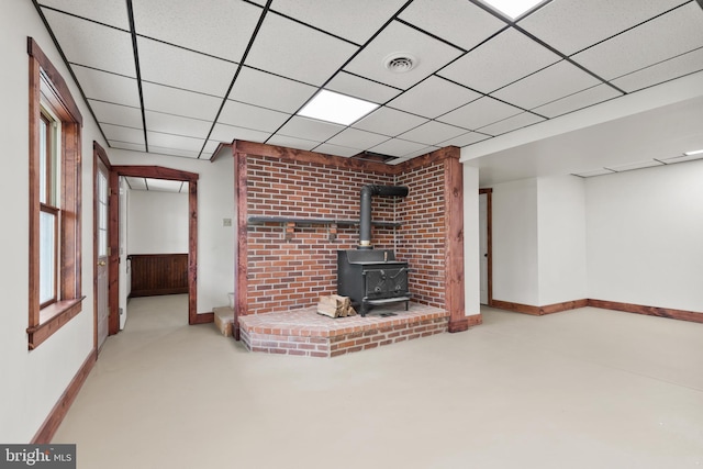unfurnished living room with a wood stove, concrete floors, a paneled ceiling, baseboards, and visible vents