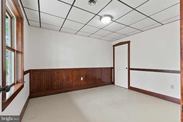spare room with finished concrete floors, a drop ceiling, visible vents, and a wainscoted wall