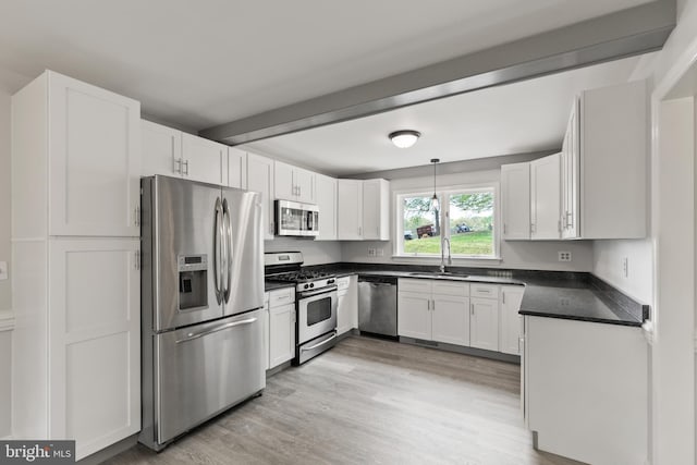 kitchen featuring dark countertops, light wood-type flooring, white cabinetry, a sink, and appliances with stainless steel finishes