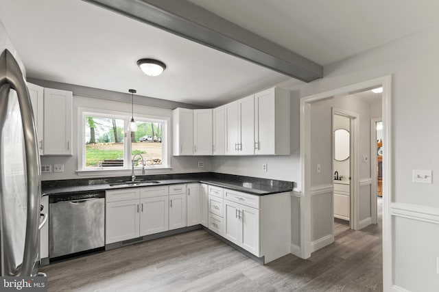 kitchen featuring dark countertops, a sink, white cabinets, stainless steel appliances, and light wood-style flooring