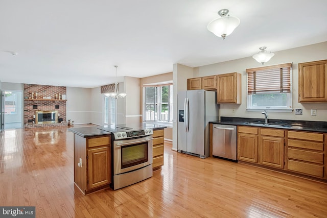 kitchen featuring a sink, light wood-style floors, a brick fireplace, dark countertops, and stainless steel appliances