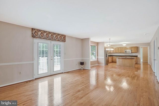 unfurnished living room with baseboards, french doors, light wood finished floors, and an inviting chandelier