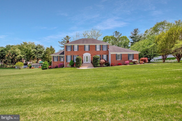 colonial inspired home with brick siding and a front yard