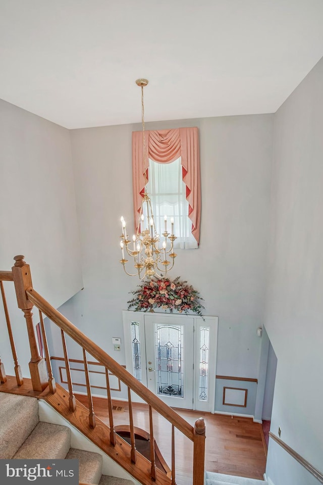 stairway with an inviting chandelier, a towering ceiling, plenty of natural light, and wood finished floors