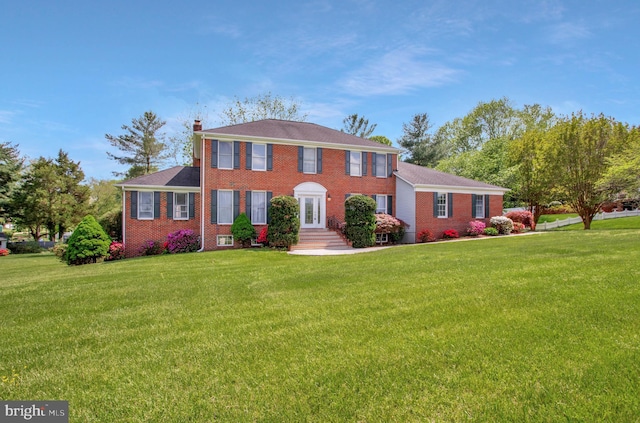 colonial house featuring brick siding, a front lawn, and a chimney