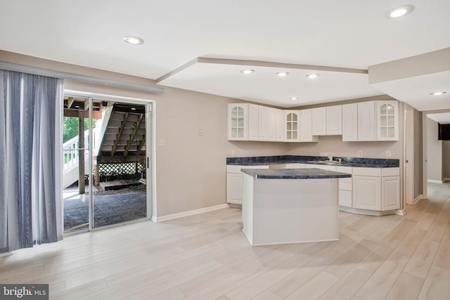 kitchen with dark countertops, light wood-style flooring, a kitchen island, and baseboards