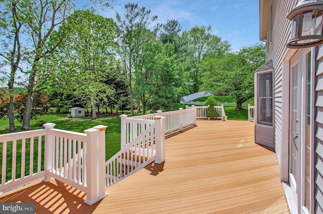 wooden terrace featuring an outdoor structure, a lawn, and a shed