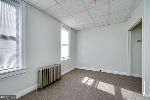 unfurnished bedroom with radiator heating unit, baseboards, a paneled ceiling, and carpet flooring