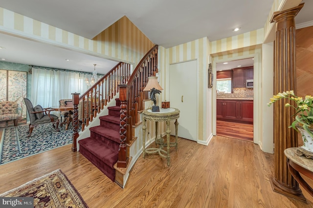 stairs with wood finished floors, a chandelier, wallpapered walls, and decorative columns