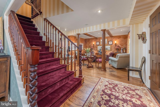 staircase featuring ornate columns, wood finished floors, and wallpapered walls