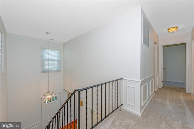corridor featuring an inviting chandelier, wainscoting, an upstairs landing, carpet flooring, and visible vents