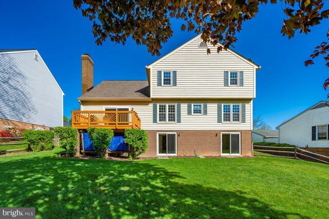 rear view of house featuring brick siding, a wooden deck, a yard, and fence
