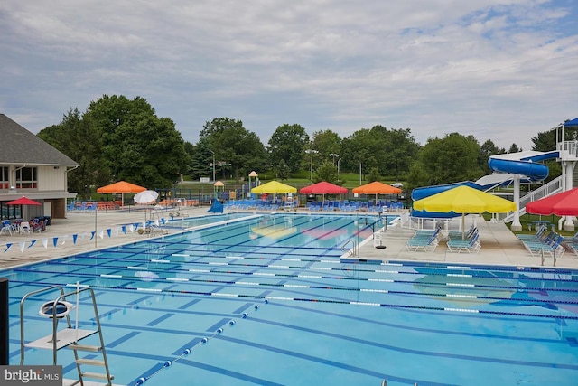 community pool featuring fence, a water slide, and a patio area