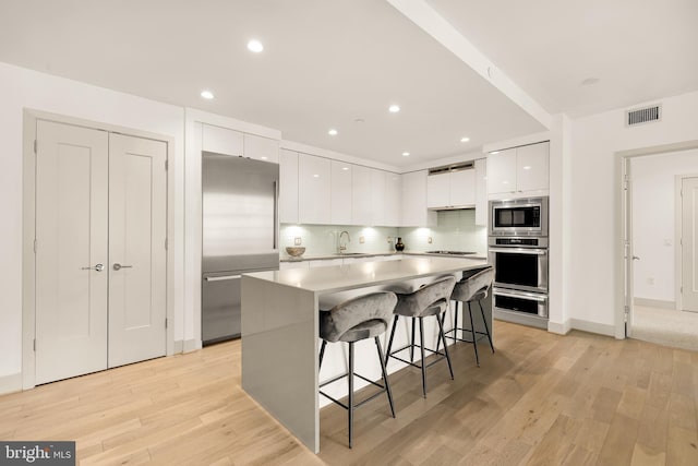 kitchen with appliances with stainless steel finishes, modern cabinets, white cabinets, a kitchen bar, and light wood-type flooring