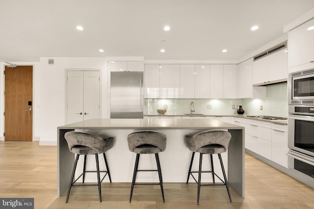 kitchen featuring modern cabinets, built in appliances, a sink, white cabinetry, and recessed lighting
