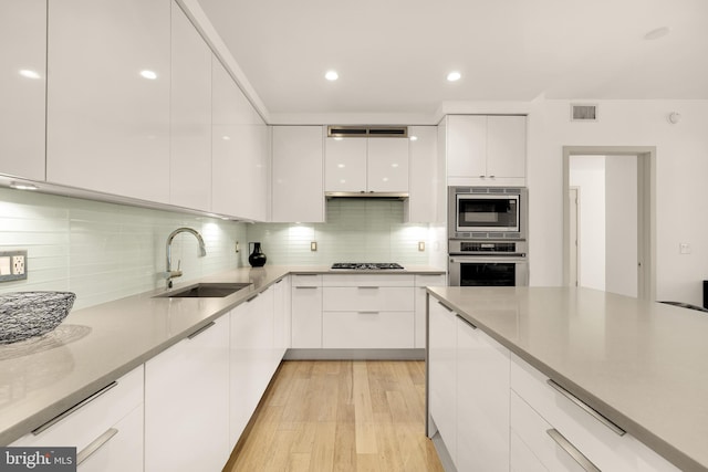 kitchen featuring appliances with stainless steel finishes, modern cabinets, a sink, white cabinetry, and light wood-style floors