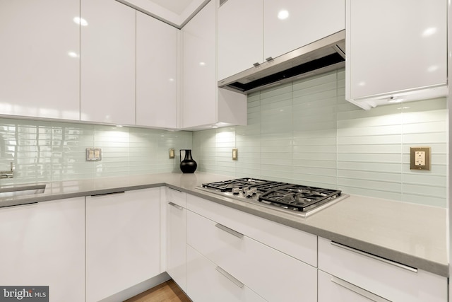 kitchen with stainless steel gas cooktop, white cabinets, under cabinet range hood, backsplash, and light countertops