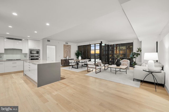 kitchen with appliances with stainless steel finishes, modern cabinets, white cabinetry, light wood-type flooring, and tasteful backsplash