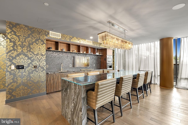 kitchen featuring open shelves, wallpapered walls, hardwood / wood-style floors, a sink, and a kitchen breakfast bar