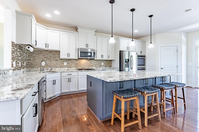kitchen with dark wood-style flooring, appliances with stainless steel finishes, a sink, white cabinetry, and a kitchen island