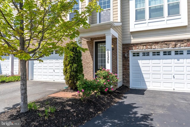 view of exterior entry with brick siding, an attached garage, driveway, and stone siding