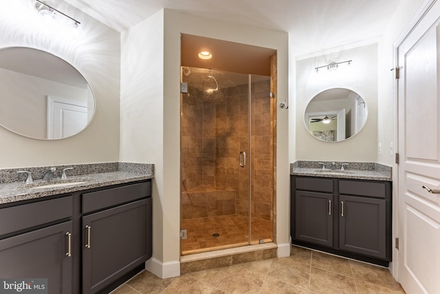 full bathroom featuring baseboards, a sink, two vanities, and a shower stall