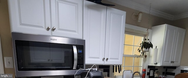 interior details featuring white cabinets, stainless steel microwave, and crown molding
