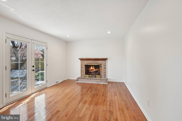 unfurnished living room featuring visible vents, light wood-style floors, french doors, and a fireplace