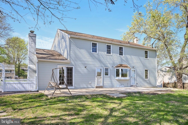 back of property featuring fence, a chimney, a lawn, and a patio