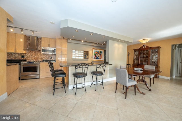 kitchen featuring dark countertops, appliances with stainless steel finishes, wall chimney range hood, and a breakfast bar