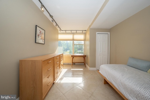 bedroom featuring a closet, rail lighting, baseboards, and light tile patterned floors