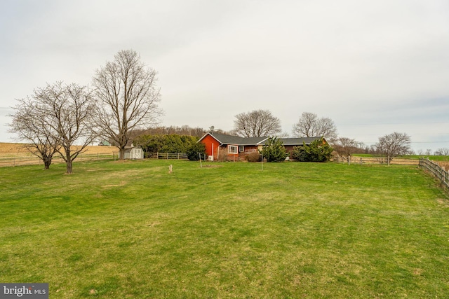 view of yard featuring a storage shed, a rural view, fence, and an outbuilding