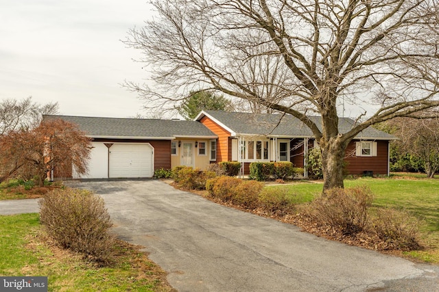 view of front of house with roof with shingles, an attached garage, driveway, and a front lawn