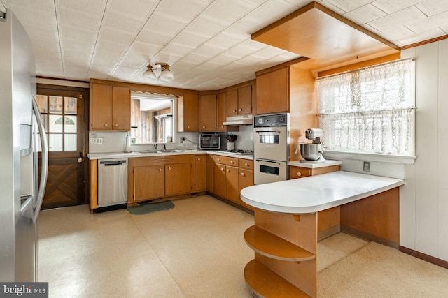 kitchen with open shelves, light countertops, a sink, a peninsula, and stainless steel appliances