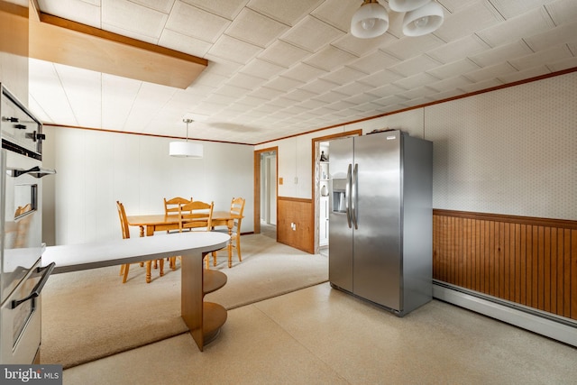 kitchen featuring light floors, wooden walls, stainless steel fridge, a baseboard heating unit, and a wainscoted wall