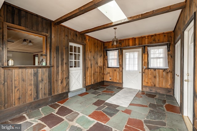 foyer entrance featuring a skylight, wood walls, beam ceiling, and stone finish flooring