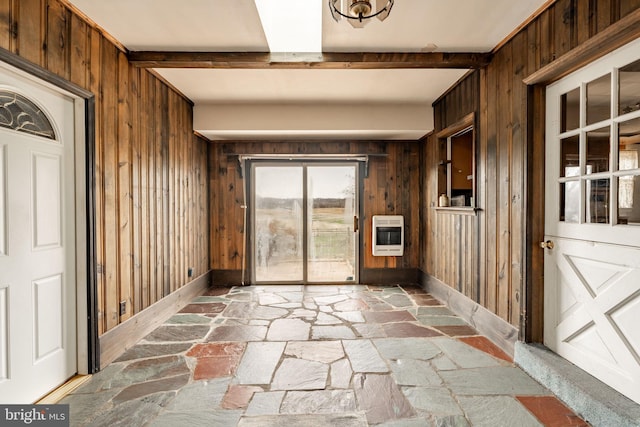 doorway to outside with baseboards, heating unit, wooden walls, and stone floors