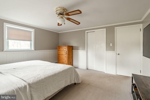 bedroom featuring a closet, crown molding, wainscoting, light carpet, and a ceiling fan