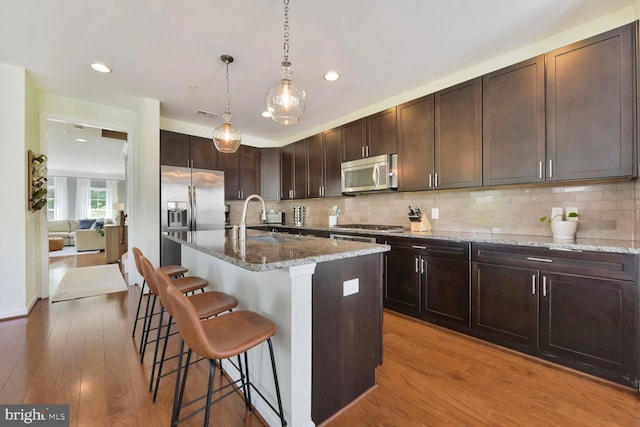 kitchen with a breakfast bar, light stone counters, stainless steel appliances, decorative backsplash, and wood finished floors