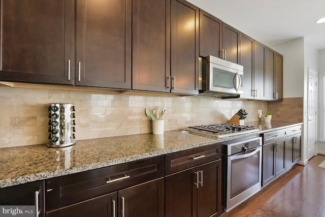 kitchen featuring dark brown cabinetry, light stone countertops, tasteful backsplash, dark wood finished floors, and stainless steel appliances