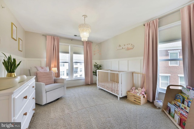 carpeted bedroom with a nursery area, an inviting chandelier, a wainscoted wall, and a decorative wall