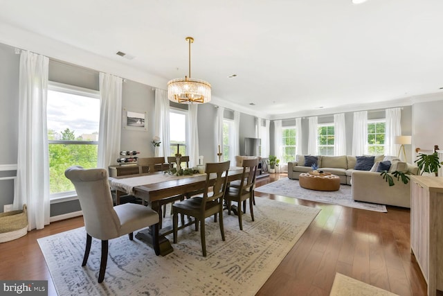 dining space featuring an inviting chandelier, ornamental molding, wood finished floors, and visible vents
