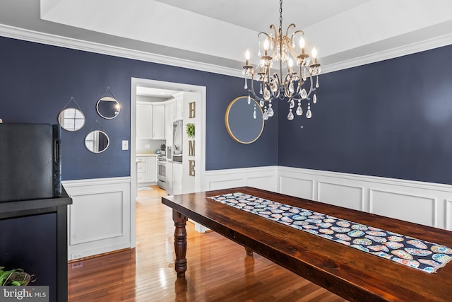 dining space featuring crown molding, a wainscoted wall, a notable chandelier, and wood finished floors