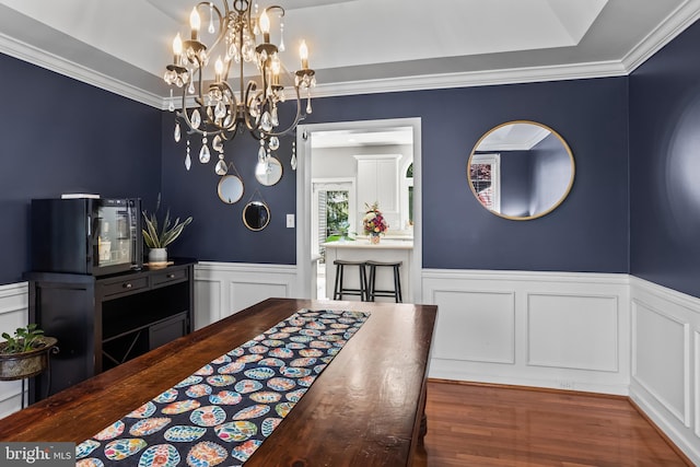 dining space featuring wood finished floors, an inviting chandelier, a decorative wall, a wainscoted wall, and crown molding